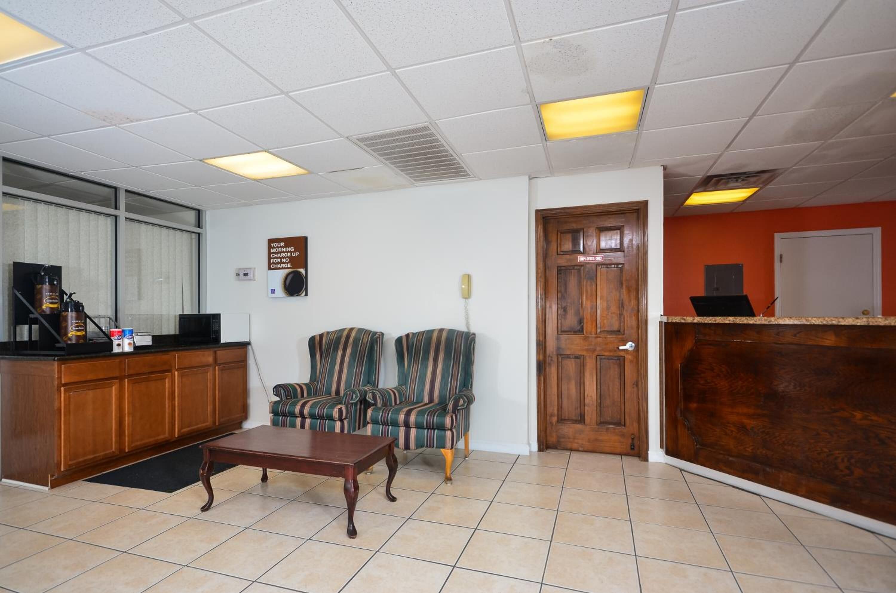 A reception area with a wooden desk, two striped armchairs, a coffee table, and a door with a sign.