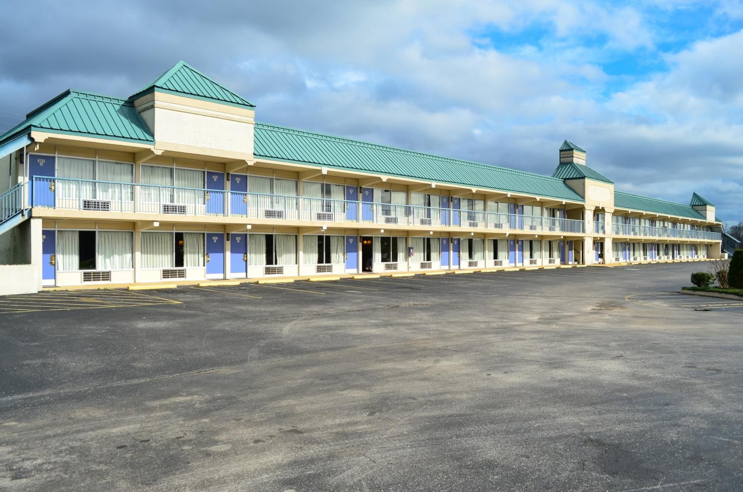 A motel with a row of rooms, a parking lot, and a green-roofed building.