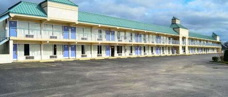 A motel with a row of rooms, a parking lot, and a green-roofed building.