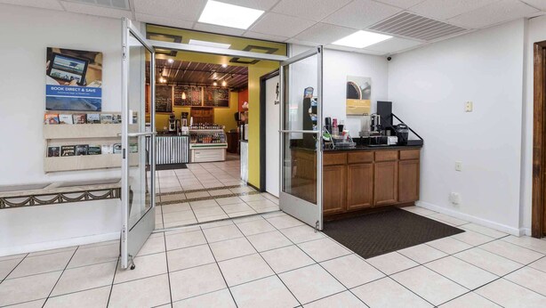 Un hall d’entrée propre et moderne, avec un comptoir de réception, un espace où l’on peut se servir du café et un tableau affichant le menu.