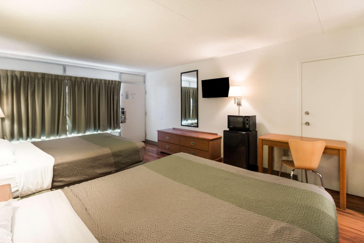 A hotel room with two beds, a desk, a chair, a television, and a dresser.