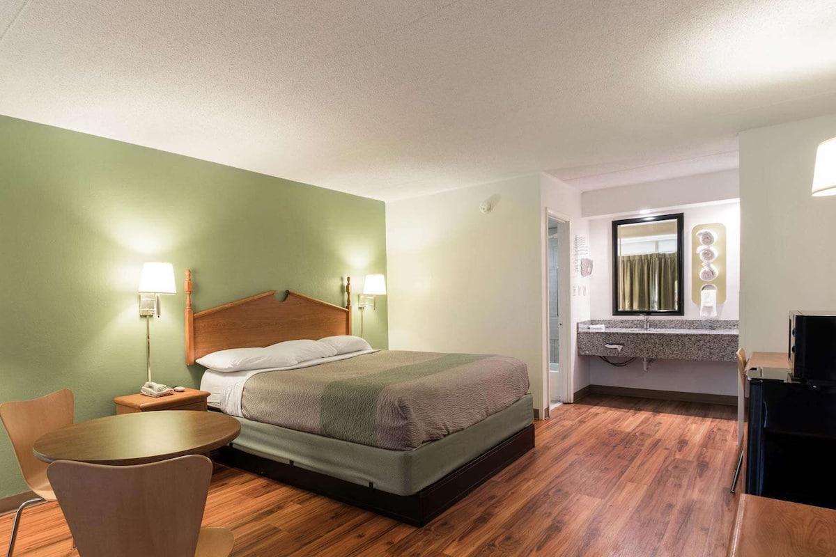 A hotel room with a bed, bedside tables, a chair, a desk, and a bathroom with a mirror and sink.