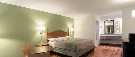 A hotel room with a bed, bedside tables, a chair, a desk, and a bathroom with a mirror and sink.
