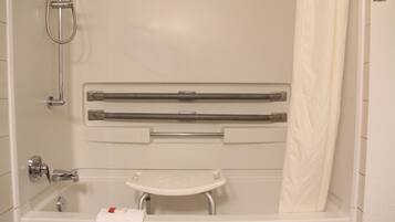 A bathroom with a bathtub, a shower, a grab bar, a small white stool, and a towel rack.