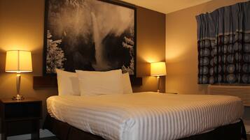 A hotel room with a large bed, two bedside lamps, a large abstract painting on the wall, and a window with patterned curtains.