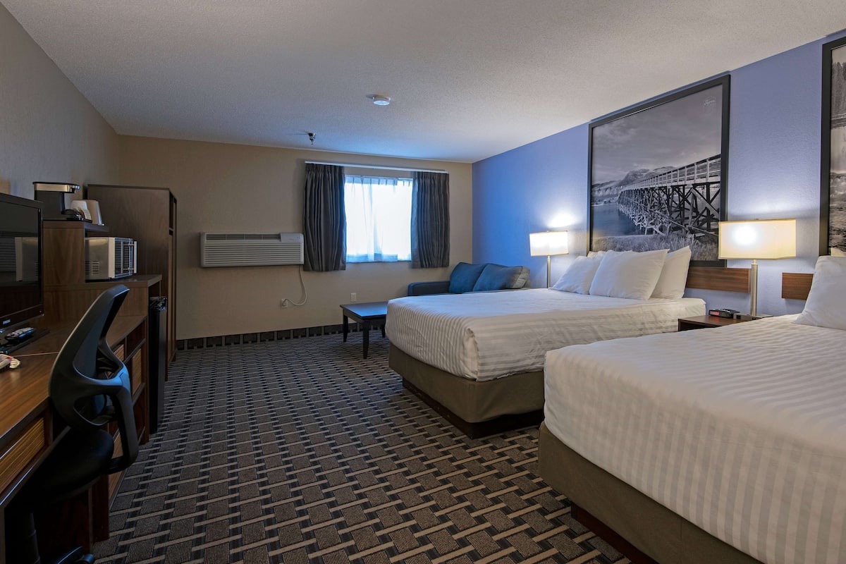 Quarto de hotel com duas camas, uma escrivaninha, televisão e uma janela grande com cortinas.