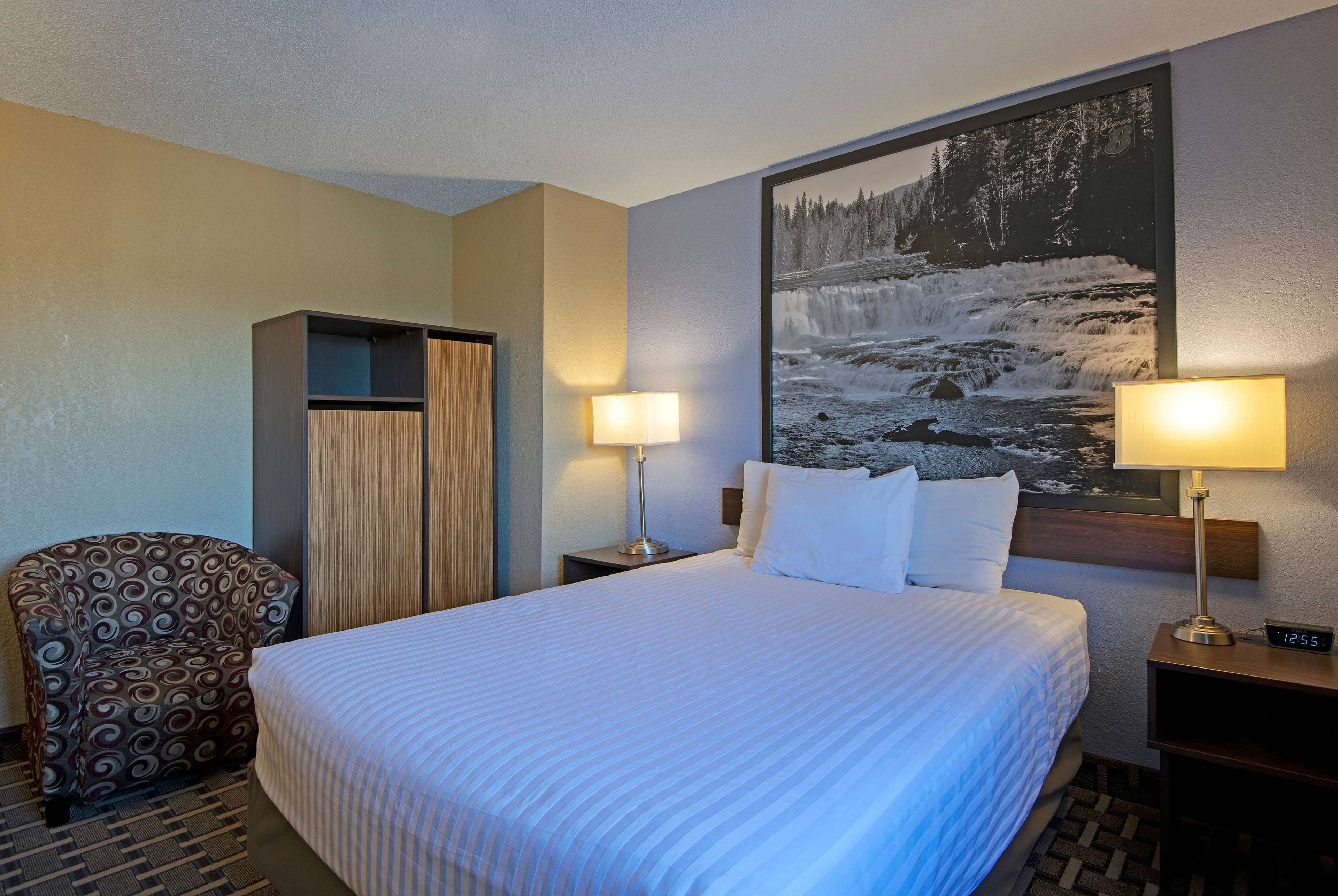 A hotel room with a large bed, two bedside tables with lamps, a chair, and a wardrobe.