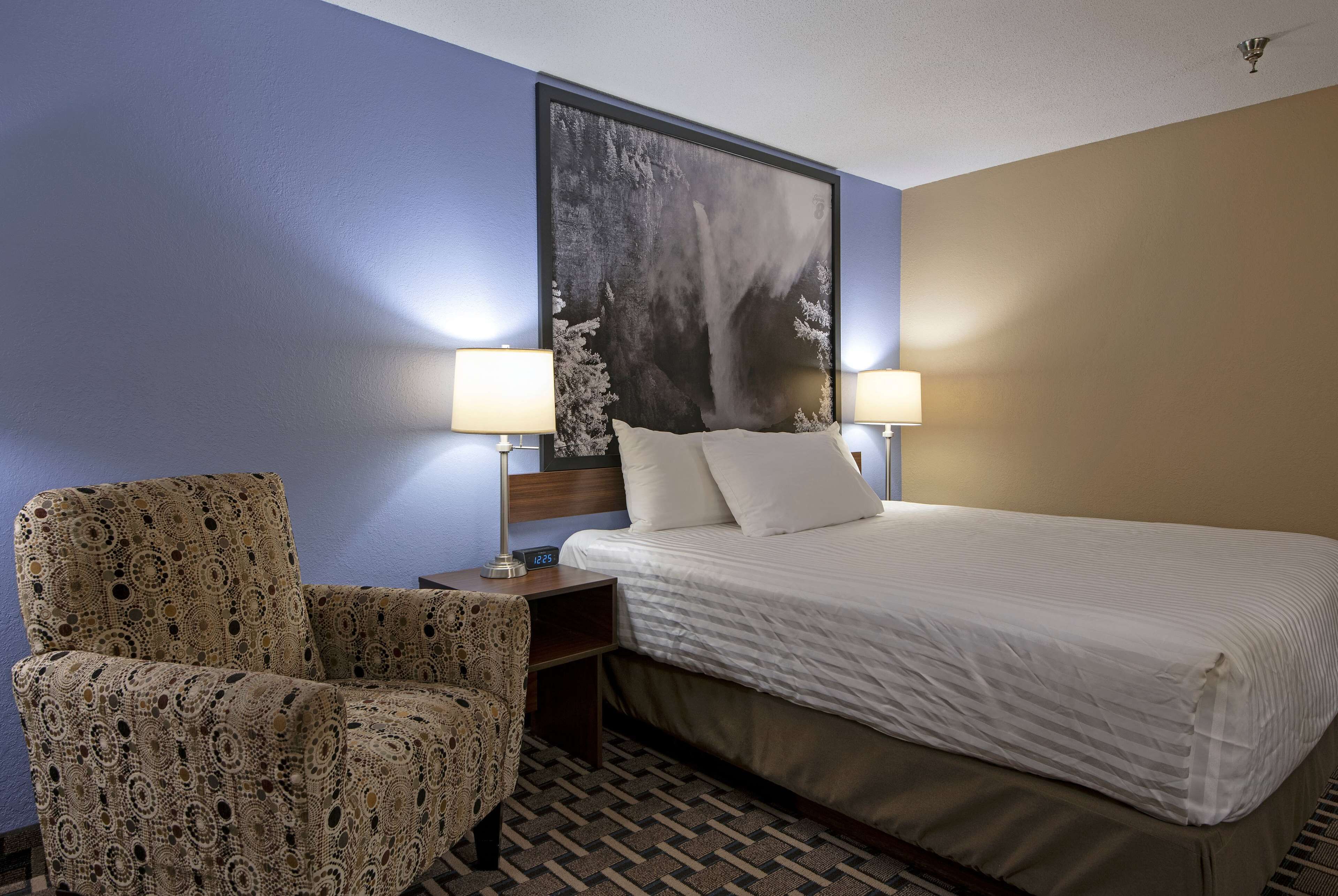 Camera d'albergo con un letto, due lampade, una poltrona a fantasia e un quadro grande appeso al muro.