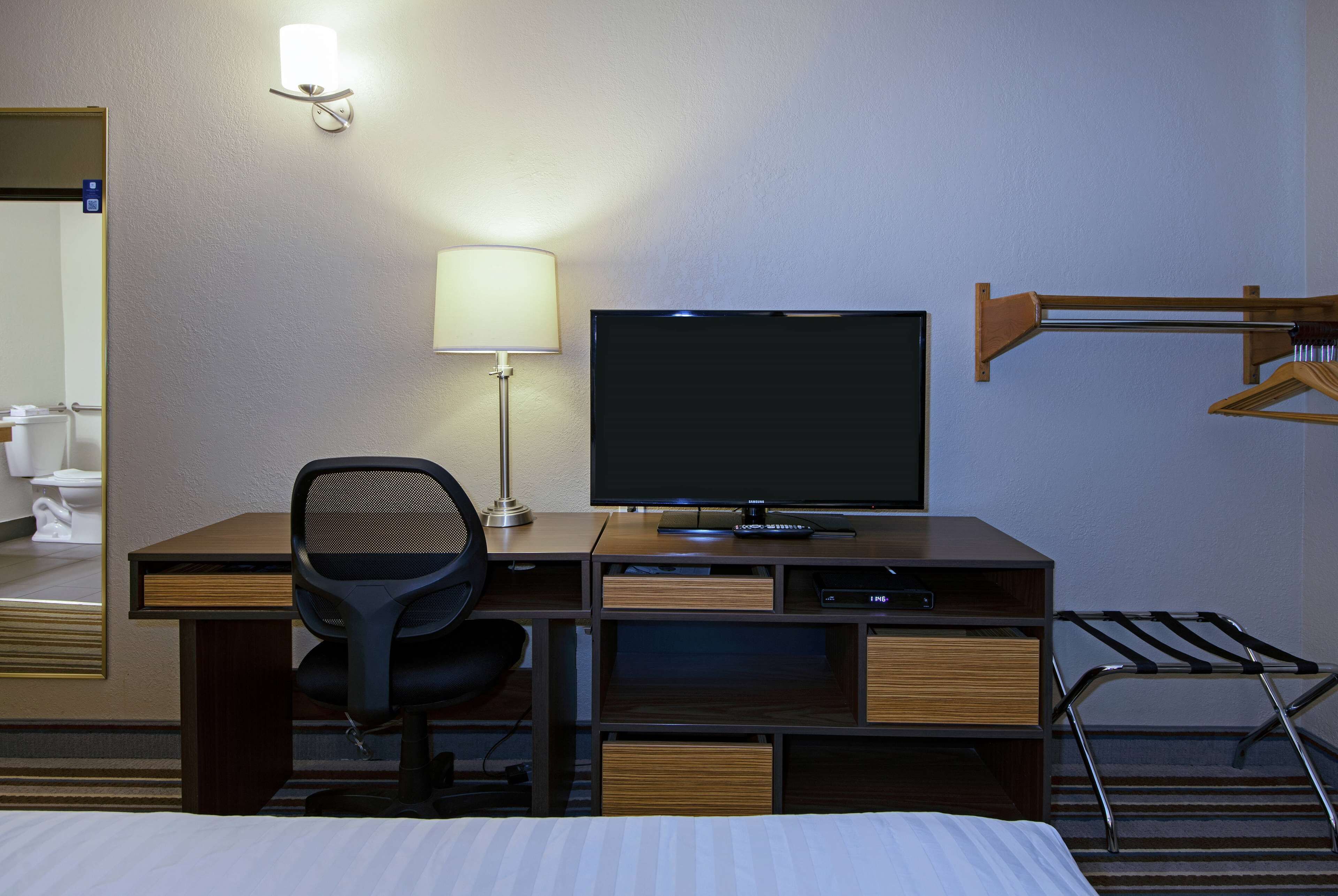 Une chambre d’hôtel comprenant un lit, un bureau avec un ordinateur, une télévision, une lampe et un porte-manteau.