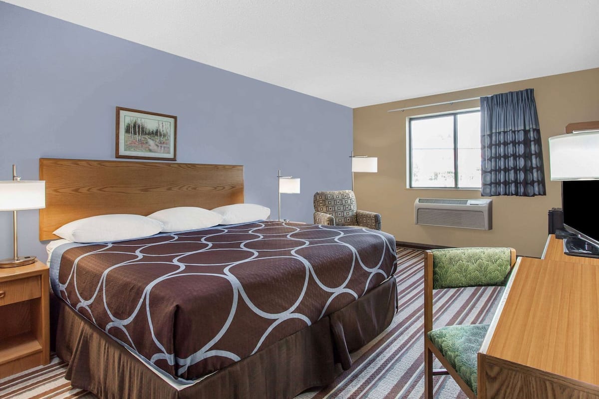 Quarto de hotel com cama grande, escrivaninha, cadeira, televisão e janela com cortinas.