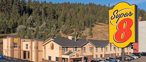 A Super 8 hotel with a parking lot and a forested hillside in the background.