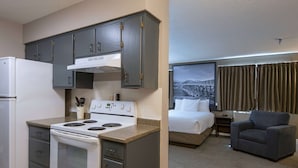 A compact kitchen with a stove and refrigerator, a bed with a view of a bridge, and a gray armchair. - Super 8 by Wyndham Kamloops On The Hill (Kamloops)
