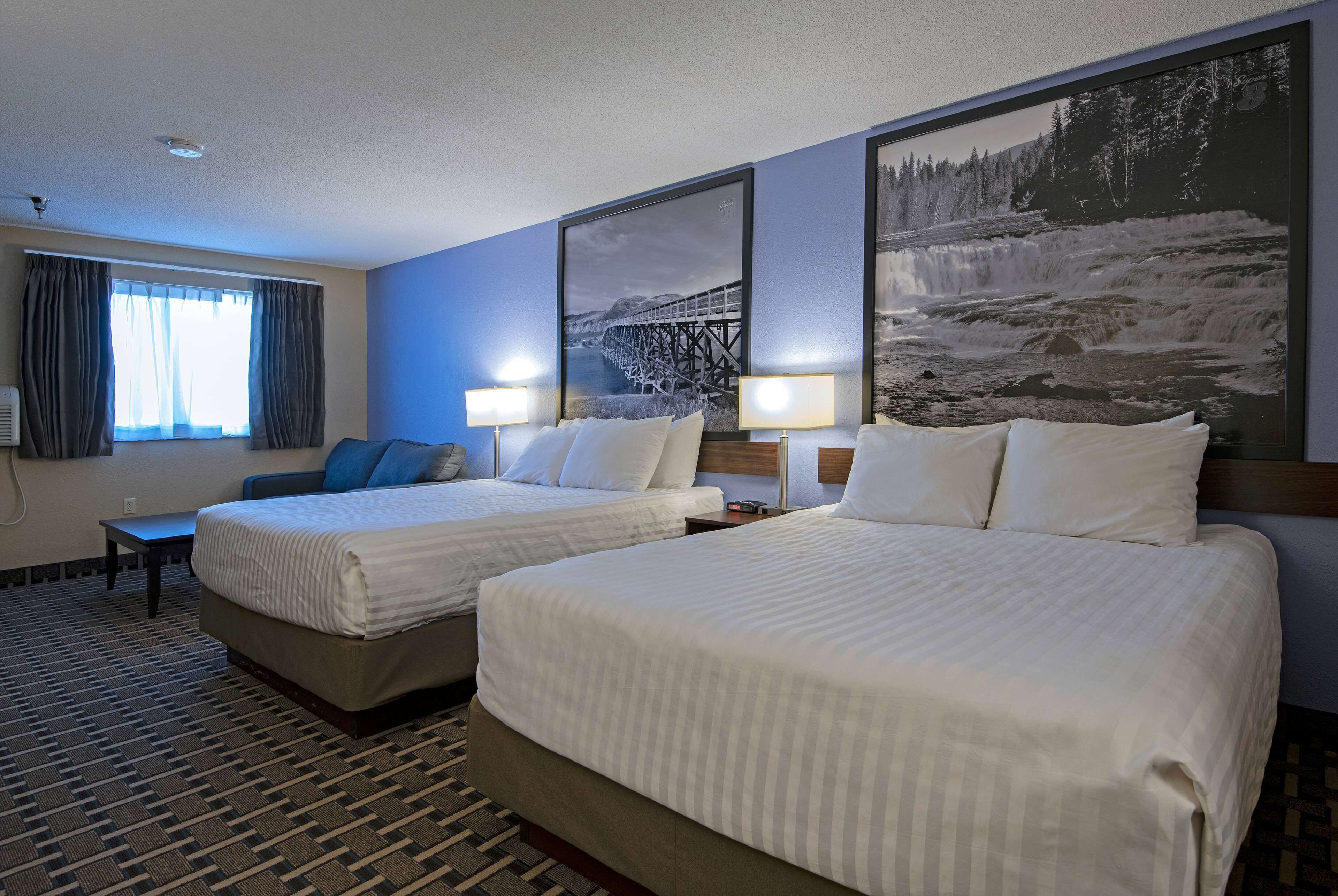 A hotel room with two beds, a large window with curtains, and wall art depicting a bridge and a waterfall.