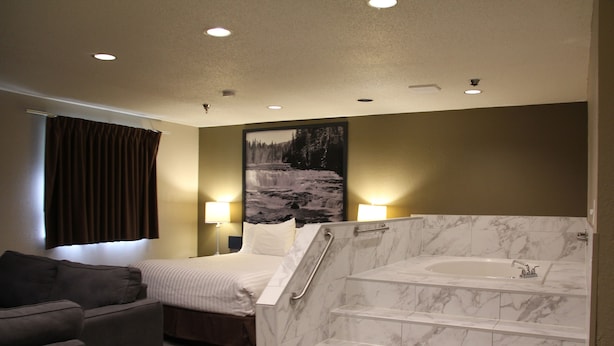 A hotel room with a bed, a sofa, a bathroom with a marble tub, and a painting on the wall. - Super 8 by Wyndham Kamloops On The Hill (Kamloops)