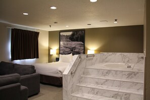 A hotel room with a bed, a sofa, a bathroom with a marble tub, and a painting on the wall. - Super 8 by Wyndham Kamloops On The Hill (Kamloops)