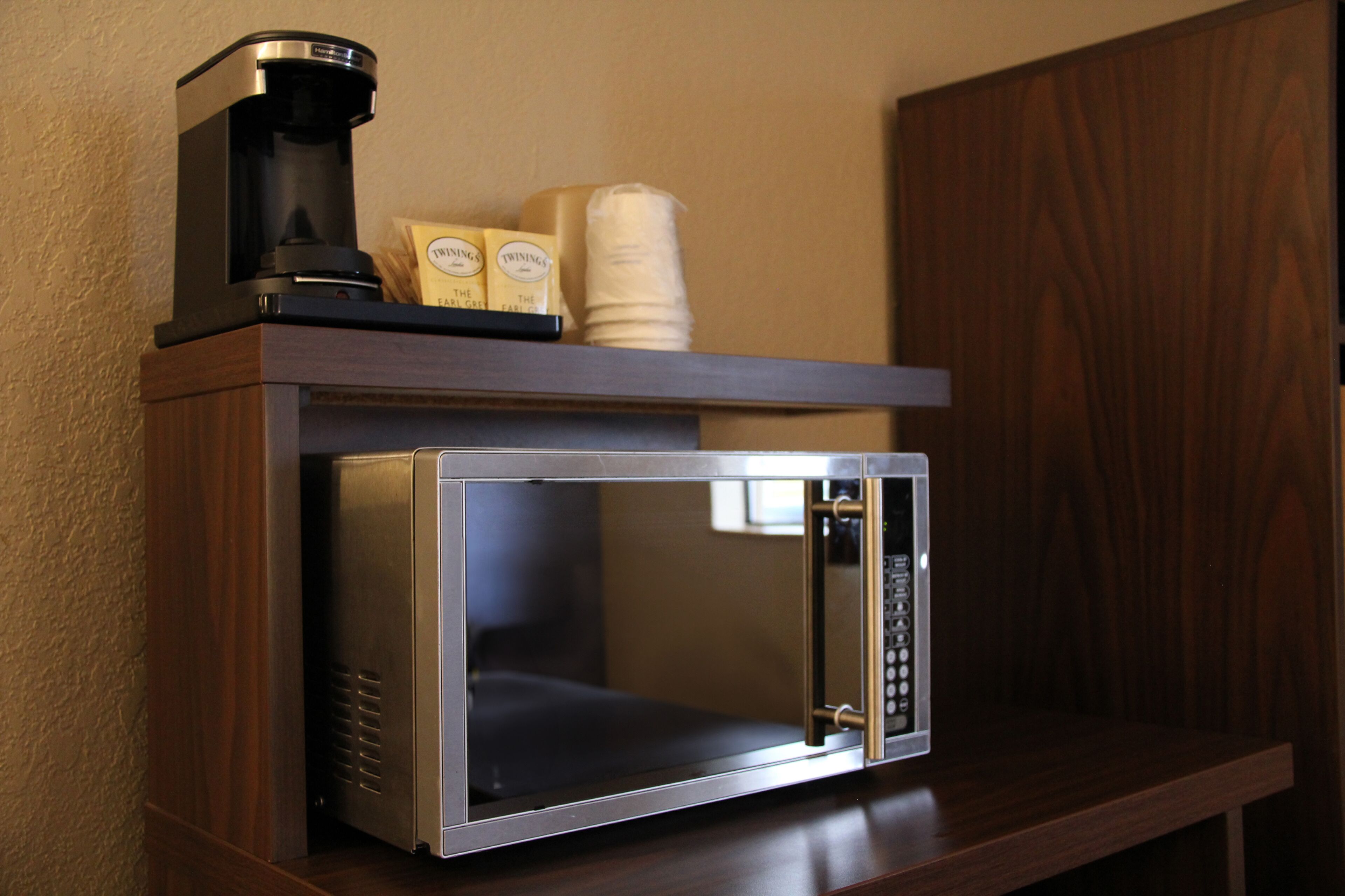 A microwave with a coffee maker and packaged snacks on a wooden shelf.