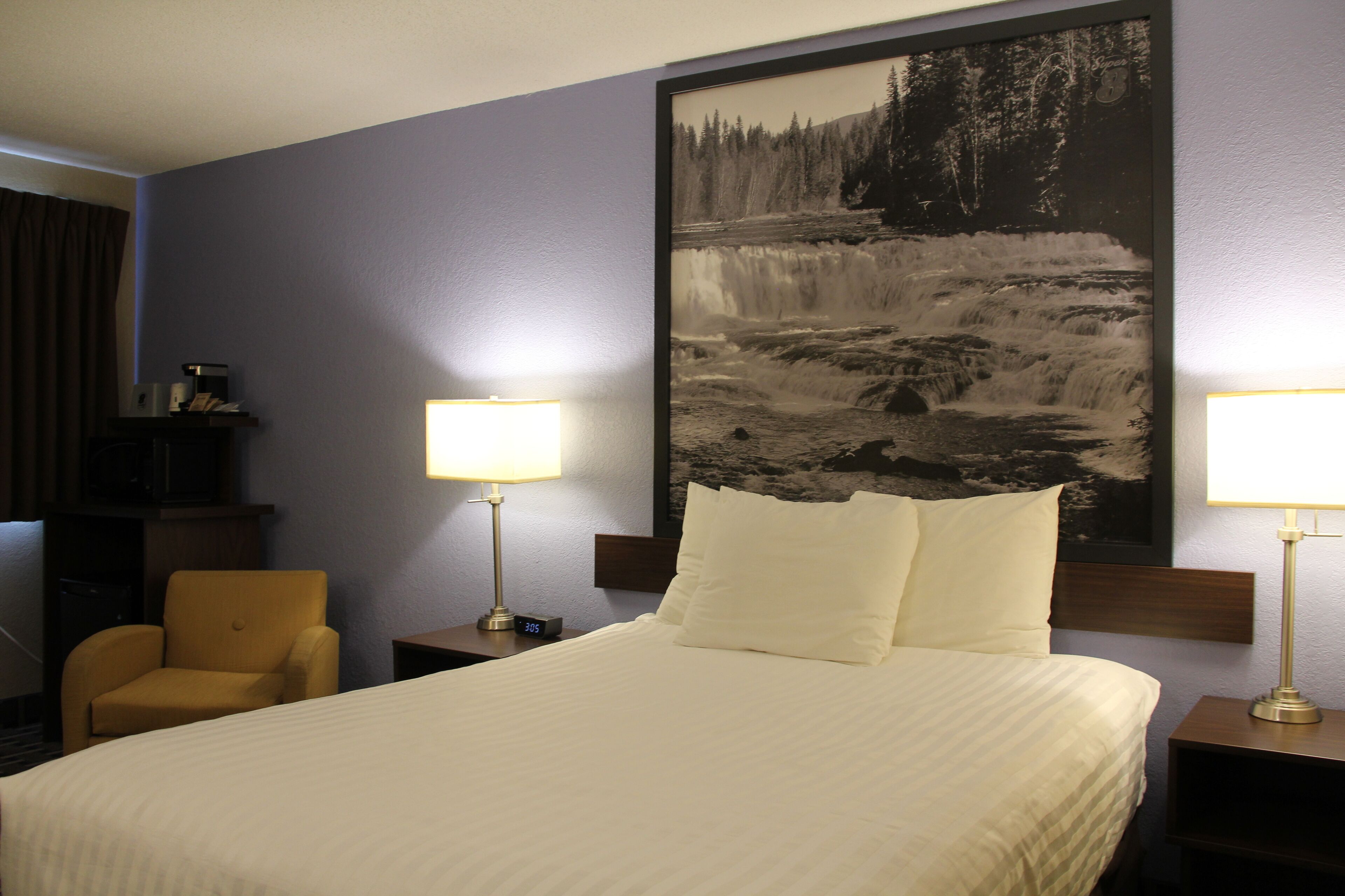 Une chambre d’hôtel avec un grand lit, deux lampes de chevet, une chaise et un tableau représentant une cascade, accroché au mur.
