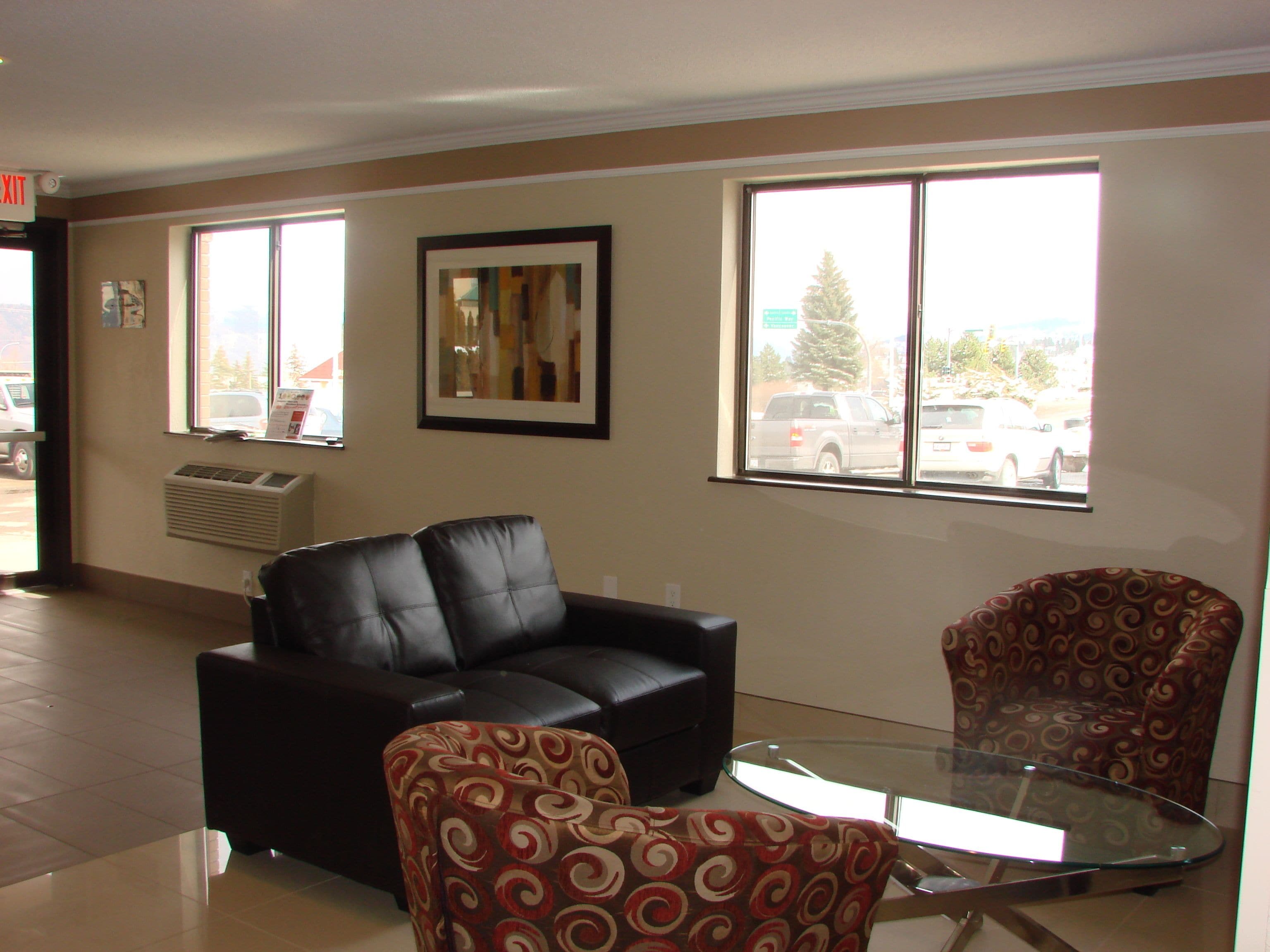 A living room with a black leather sofa, a patterned armchair, and a glass-top coffee table.