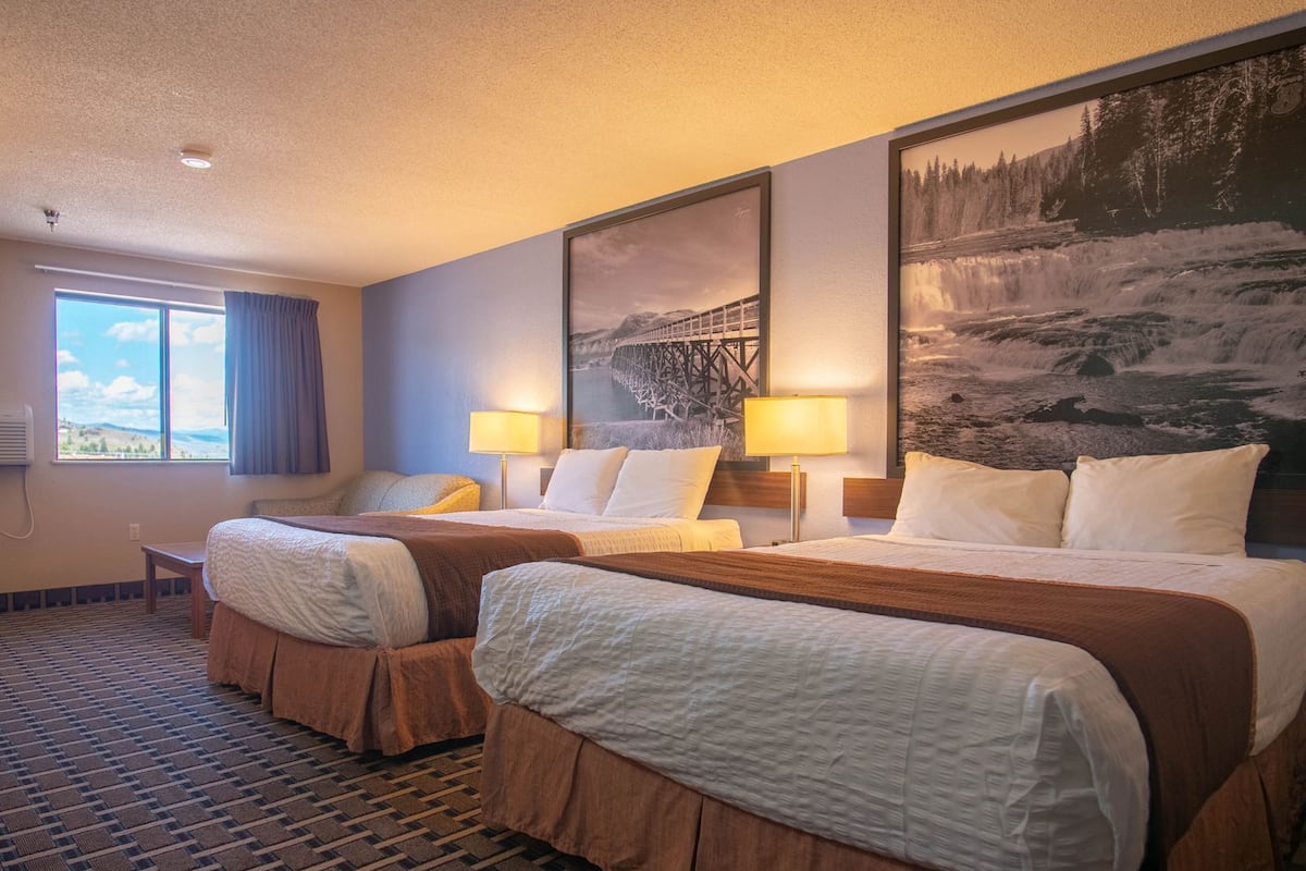 Quarto de hotel com duas camas, uma janela grande, um quadro e uma luminária.
