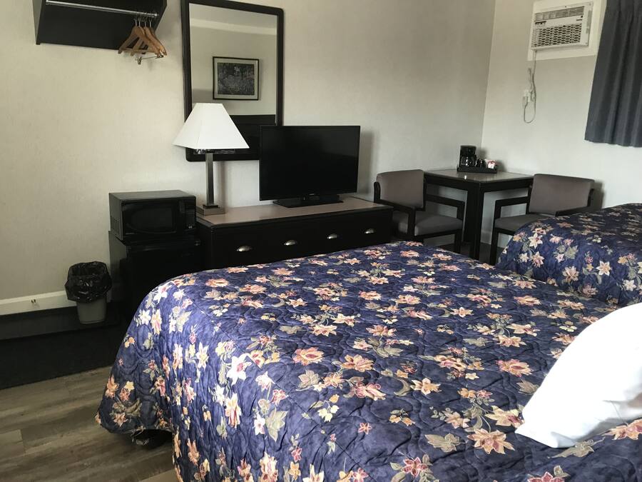 Habitación de hotel con una cama grande, un televisor, un escritorio con una silla, una lámpara y un cesto de basura.