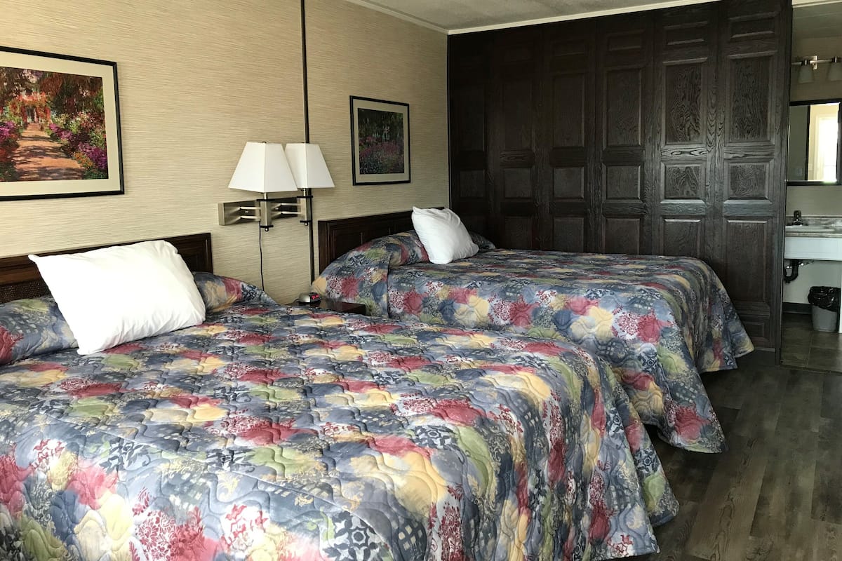 A hotel room with two beds, each with floral-patterned bedding, a nightstand with a lamp, and a large wooden door.