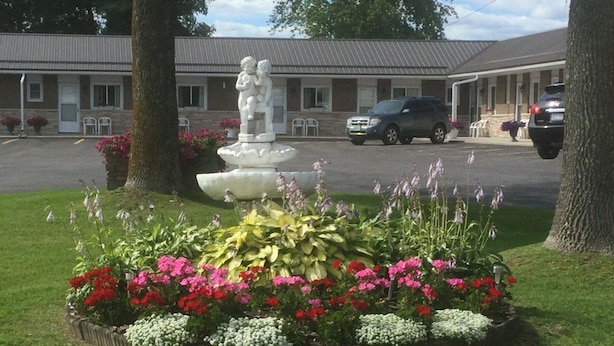 Un jardín ajardinado con una fuente y flores de colores, un edificio de motel al fondo y un coche estacionado.