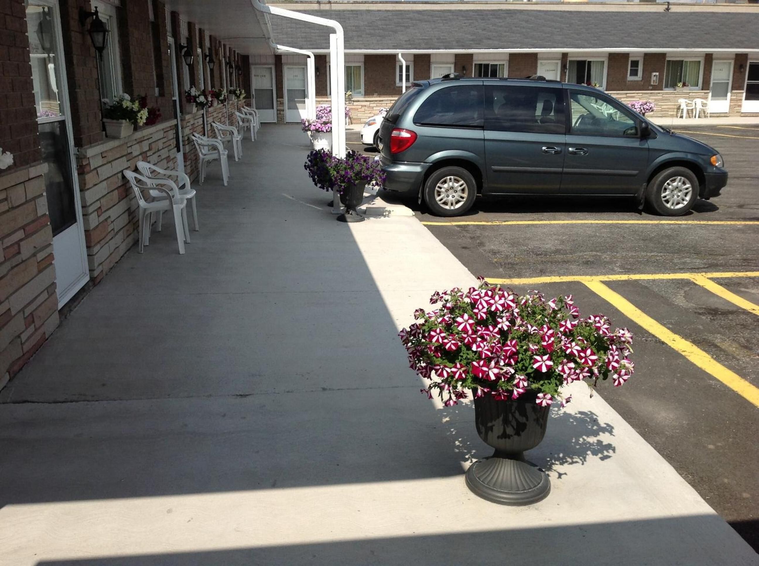A parking lot with a row of white chairs outside a building with brick walls and a covered walkway.