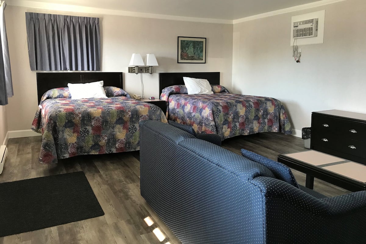 A hotel room with two beds, a desk, a chair, a lamp, and a painting on the wall.