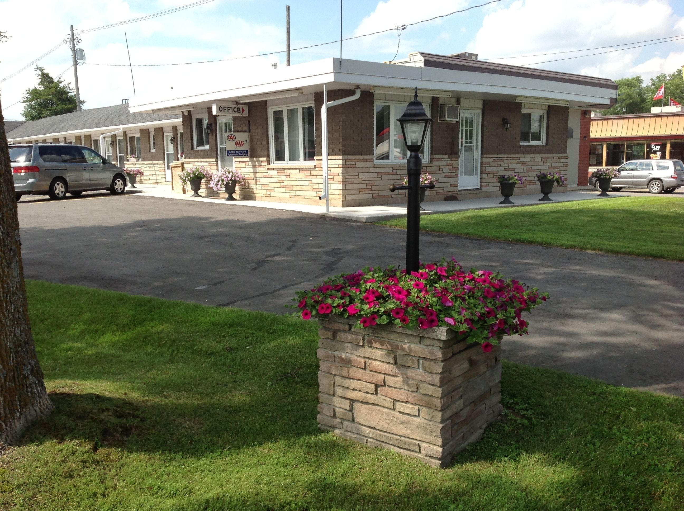 Un motel à la façade en briques, doté d’un parking couvert et agrémenté, au premier plan, d’un jardinier.