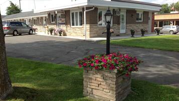 Un motel à la façade en briques, doté d’un parking couvert et agrémenté, au premier plan, d’un jardinier.