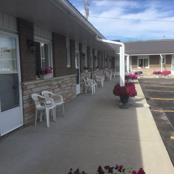 A motel with a brick facade, white-framed windows, and a covered outdoor seating area with plastic chairs.