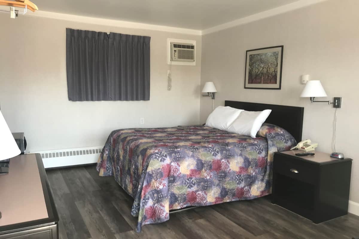 A hotel room with a bed, bedside lamps, a nightstand with a phone and remote, a desk with a lamp, and a window with curtains.