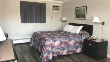 A hotel room with a bed, bedside lamps, a nightstand with a phone and remote, a desk with a lamp, and a window with curtains.