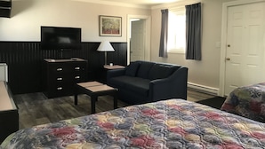 Habitación de hotel con cama, sofá, televisor, cómoda y ventana con cortinas.