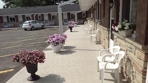 Un motel con estacionamiento, área de estar al aire libre con sillas y jardineras de flores a lo largo de la fachada.