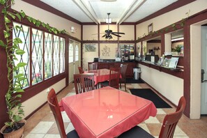 Ein Restaurant mit rotem Tisch, Holzsesseln, einem Deckenventilator und einem Blumentopf.