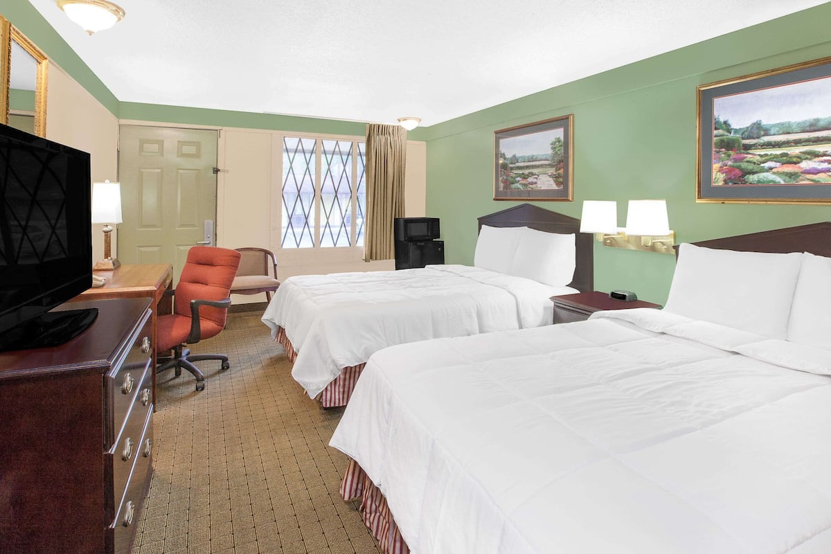 A hotel room with two beds, a desk with a TV, a chair, a window with curtains, and a painting on the wall.