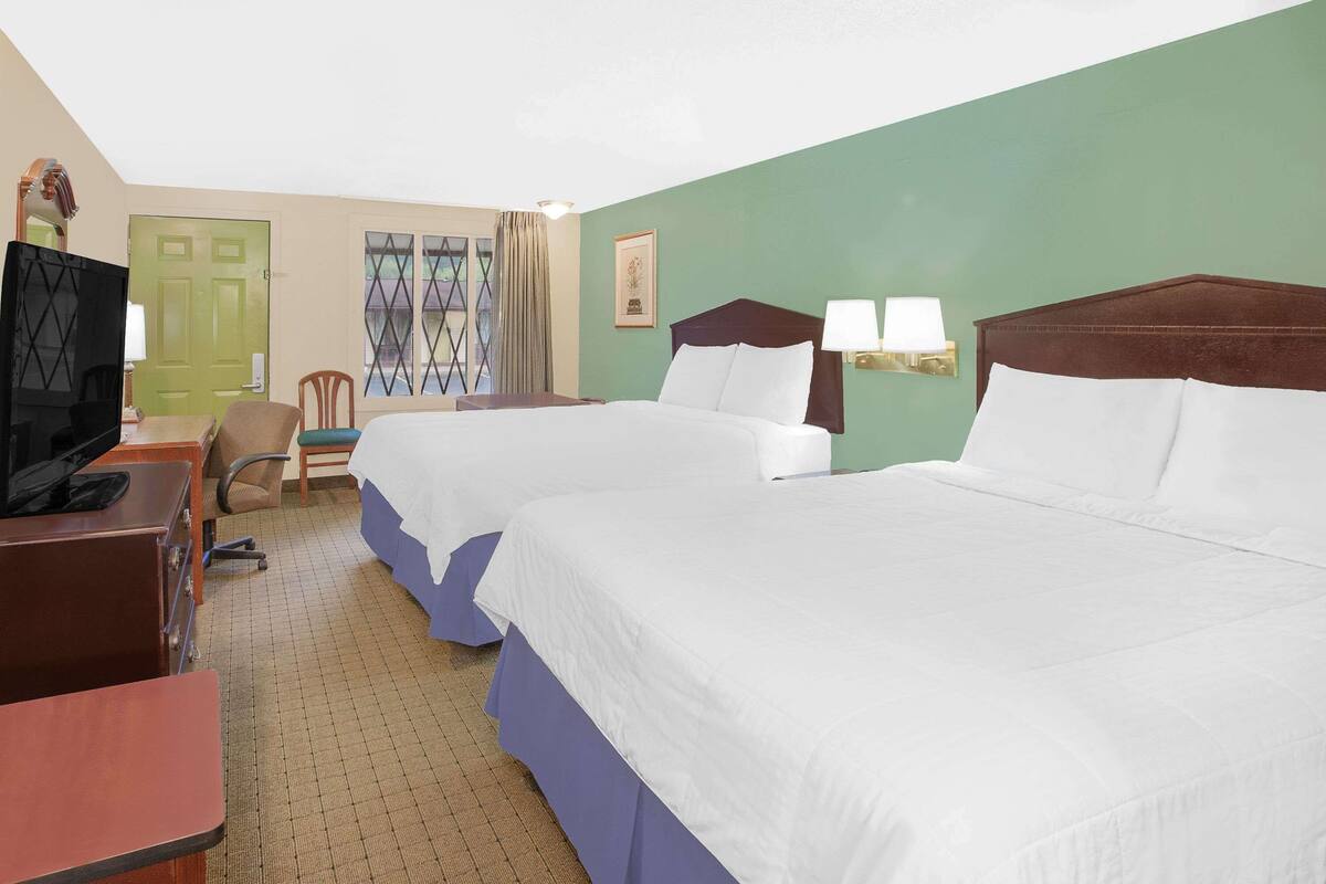 A hotel room with two beds, a desk with a television, a chair, and a door.