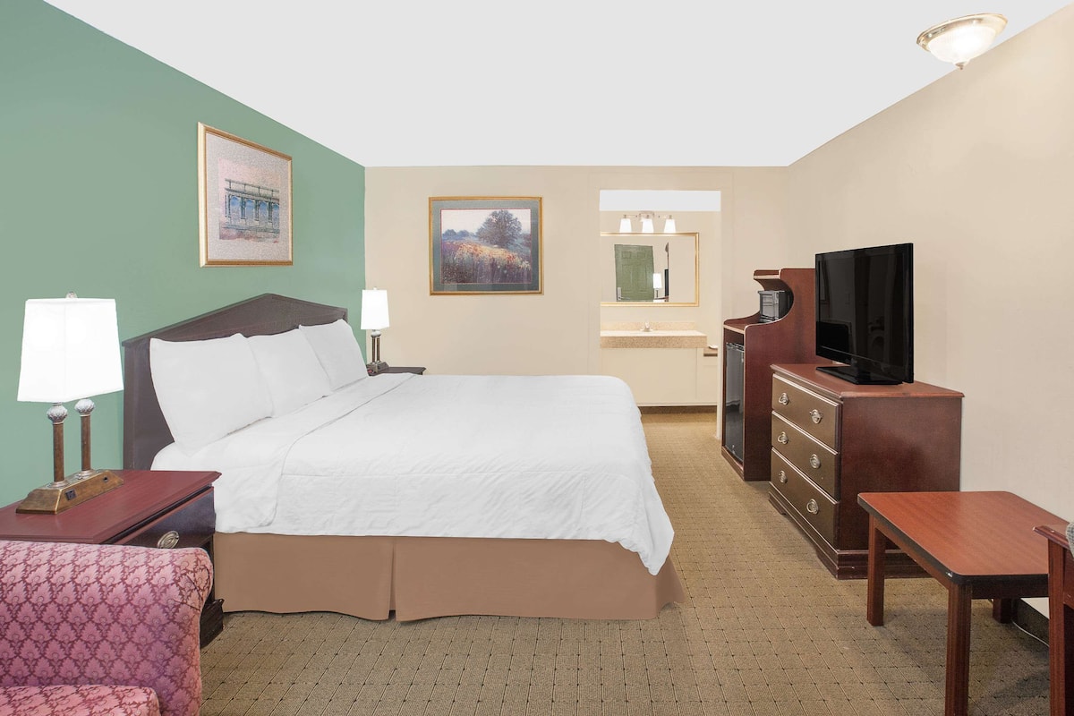 A hotel room with a bed, a desk, a television, a dresser, a chair, and a bathroom with a mirror and sink.