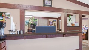 A reception desk with a coffee machine, stacked cups, and a potted plant. - Knights Inn Battle Creek (Battle Creek)