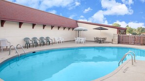 A swimming pool with a brick building in the background, outdoor seating, and a clear sky. - Knights Inn Battle Creek (Battle Creek)