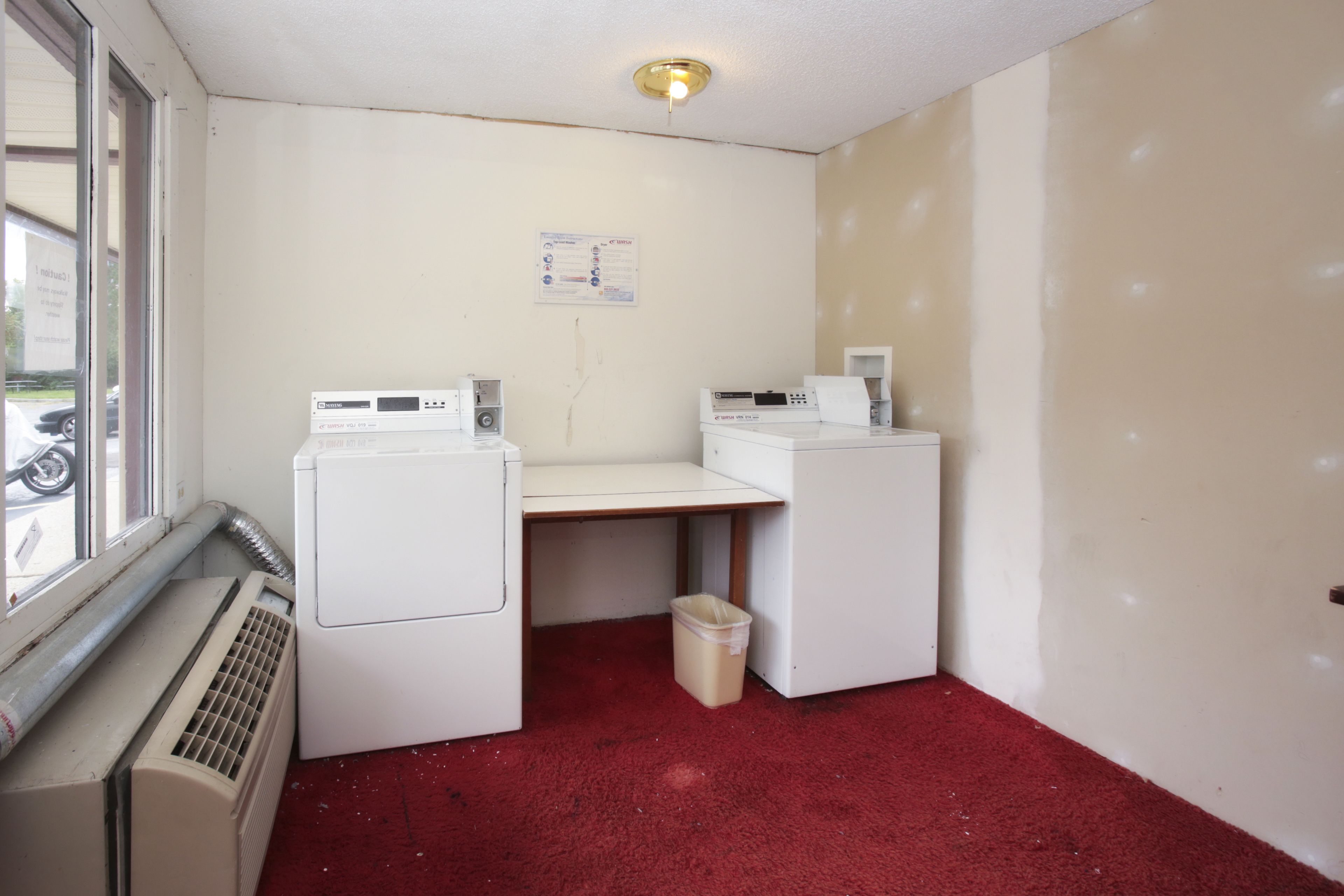 A laundry room with a washing machine, dryer, and a heater. There is a window and a bulletin board on the wall.