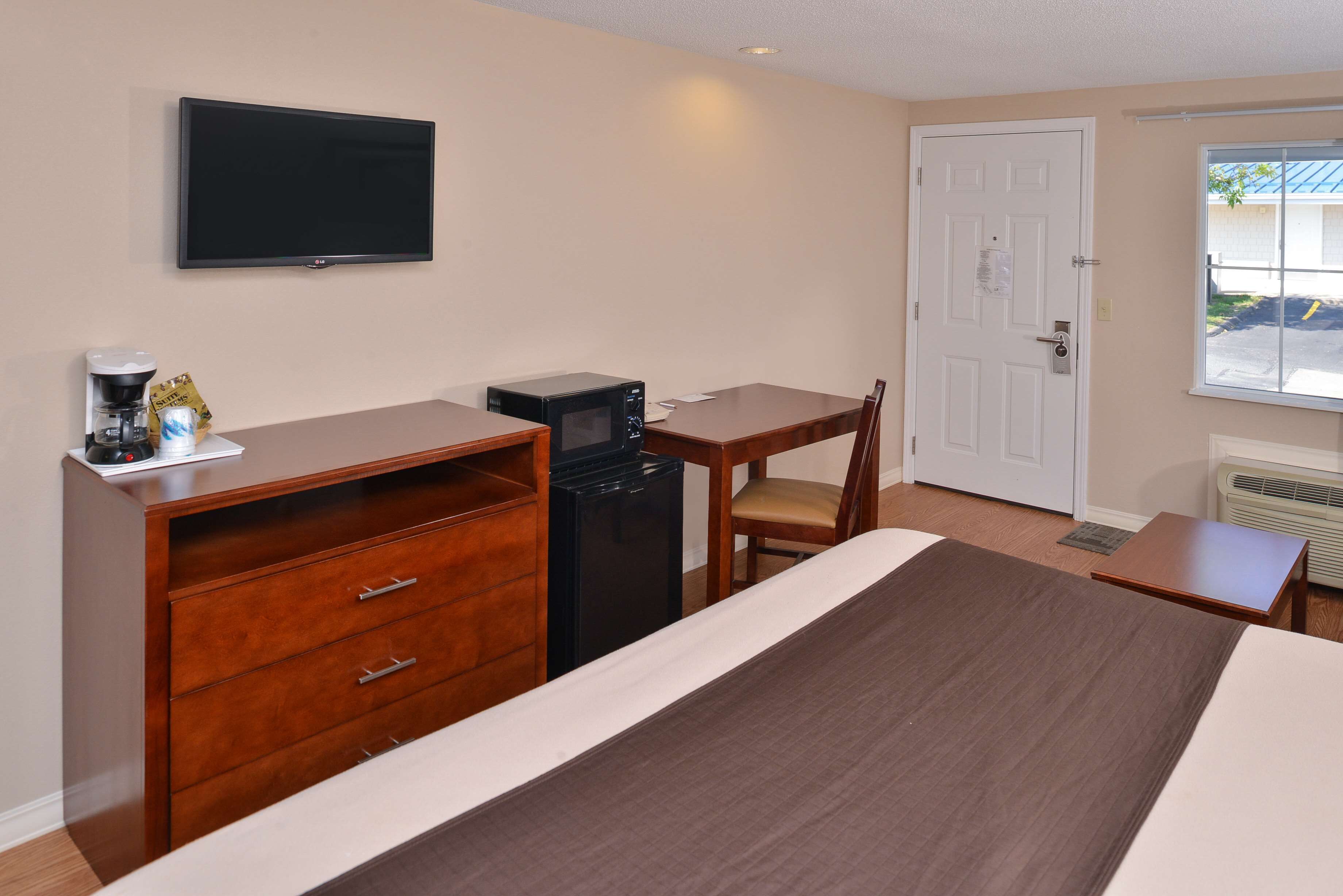 Une chambre d’hôtel équipée d’un lit, d’un bureau, d’une chaise, d’une télévision, d’une machine à café et d’un four à micro-ondes.