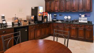 Uma cozinha com mesa de madeira, armários, máquina de café e dispensador de suco.