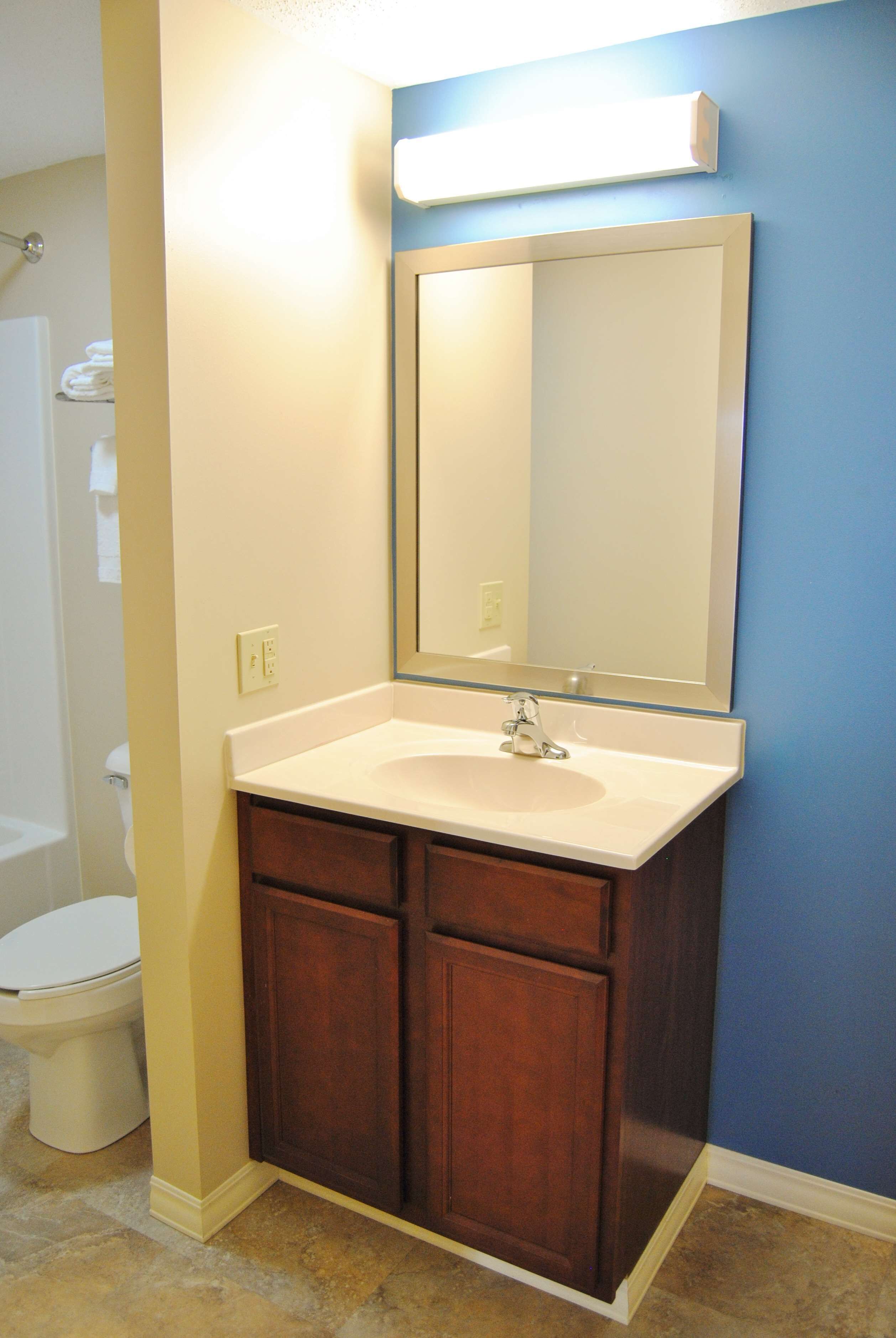 A bathroom with a white sink, dark wooden cabinets, a large mirror, and a blue wall.