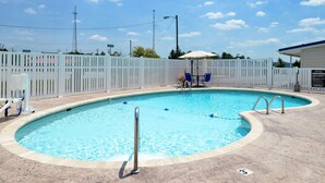 Una piscina amb una tanca blanca, una cadira de socorrista i una zona de relax amb cadires i una ombrel·la.