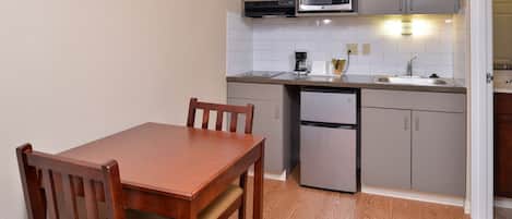 A compact kitchen with a wooden table and chairs, a microwave, a coffee maker, and a refrigerator.