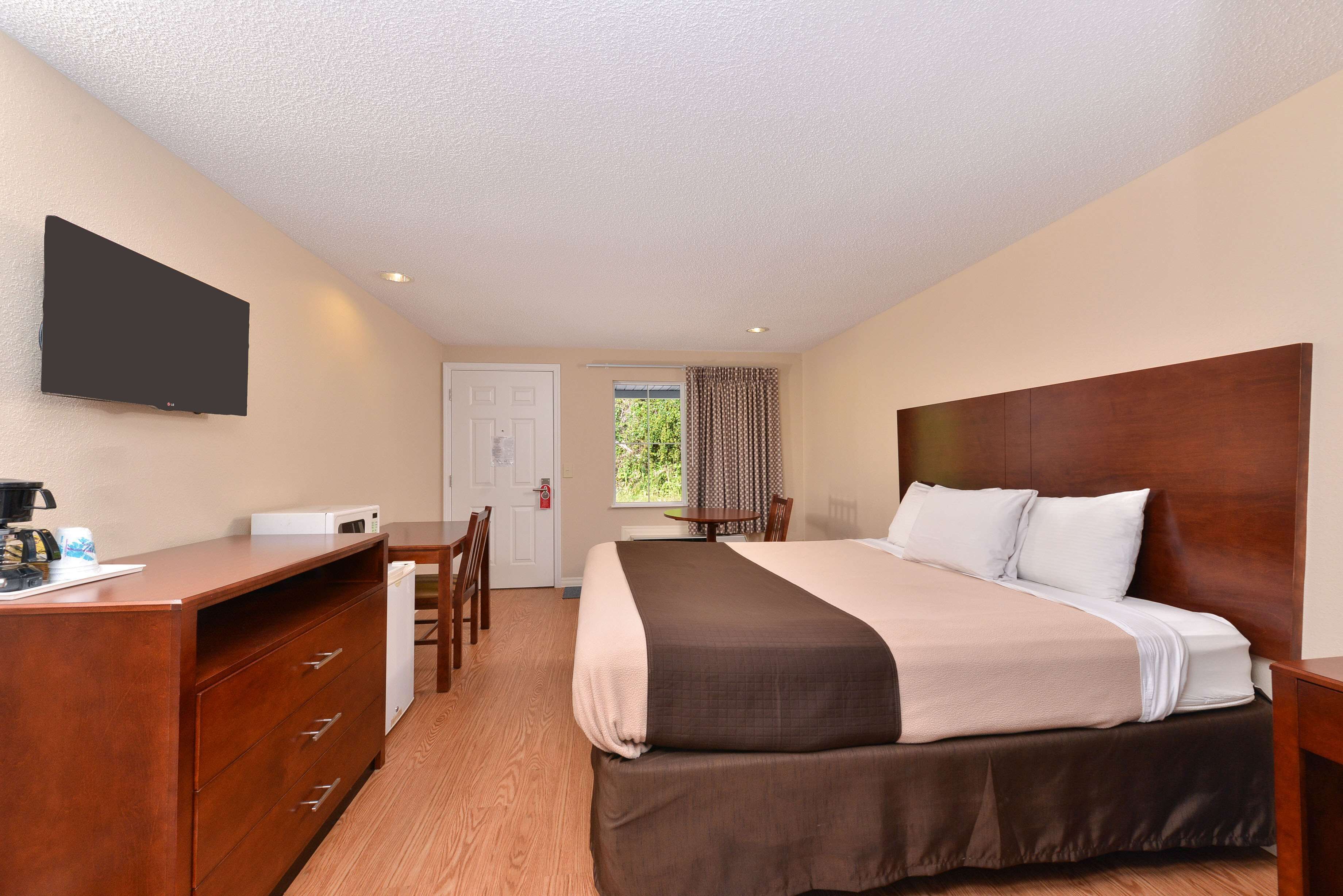 A hotel room with a bed, desk, chair, and a flat-screen TV mounted on the wall.