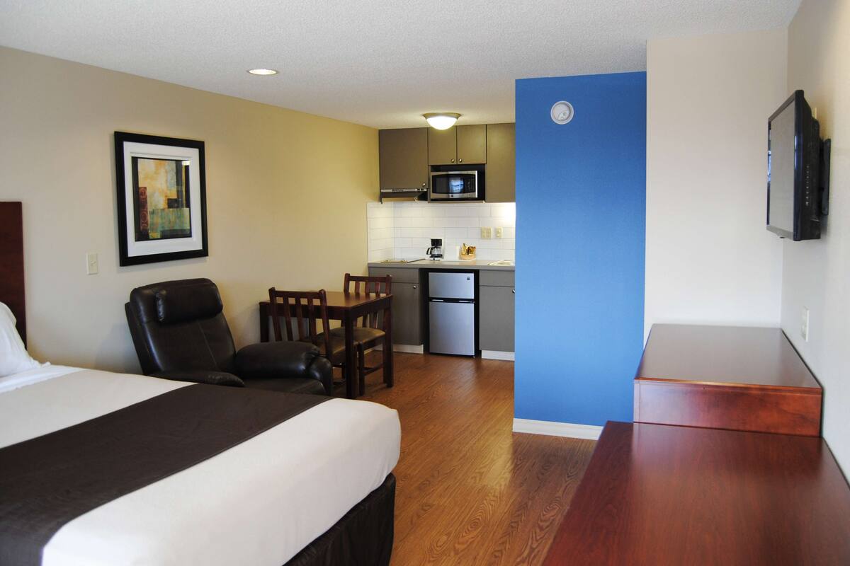 Habitación de hotel con cama, escritorio, silla, microondas, refrigerador y televisión.