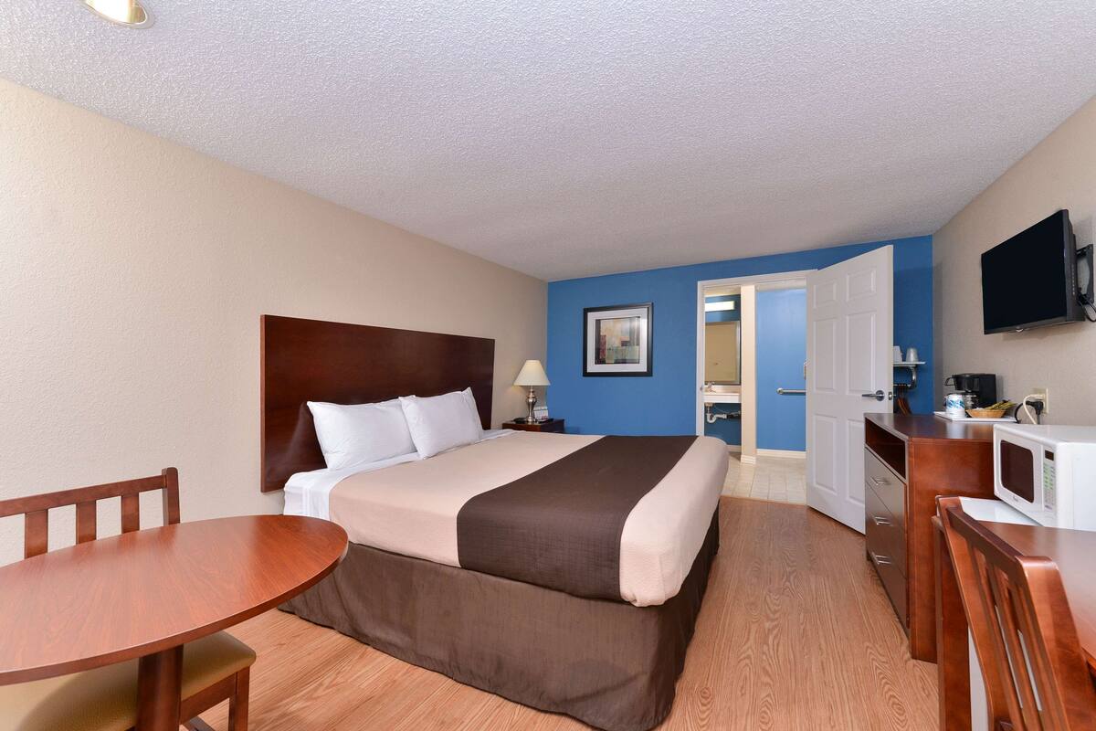 Habitación de hotel con una cama, un escritorio, una silla, un televisor y una puerta que da a un baño.